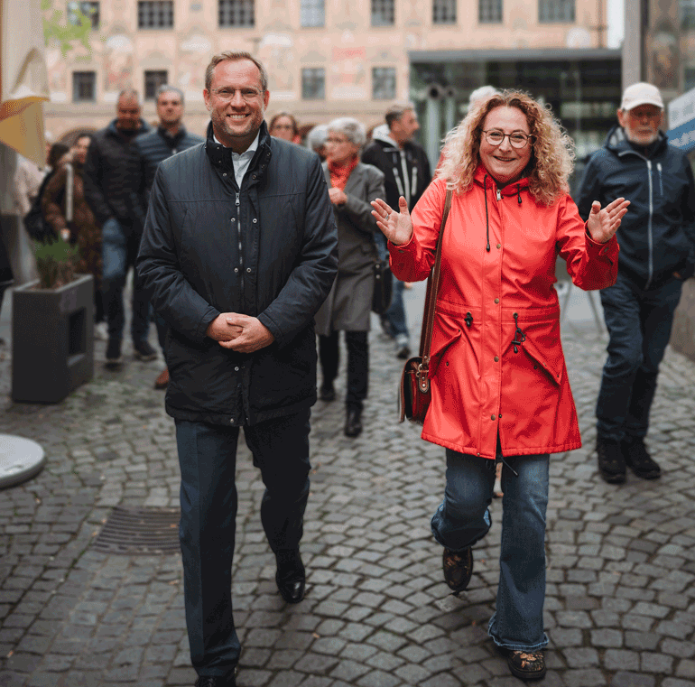 OB Ansbacher mit einer Stadtführerin in rotem Mantel. Im Hintergrund ist das Rathaus zu sehen.